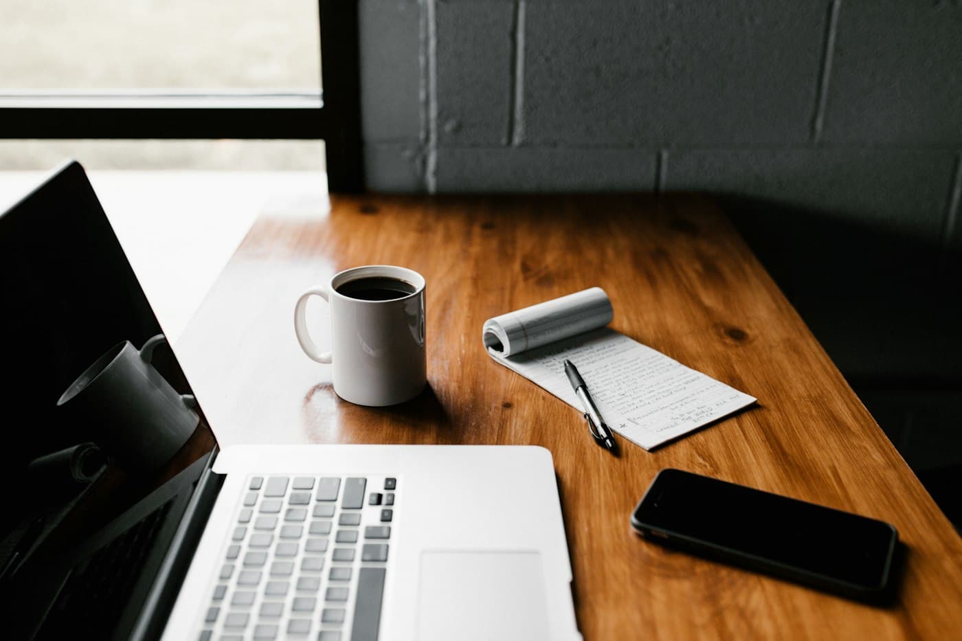 A laptop, notebook and coffee on a wooden desk, ready for focused work